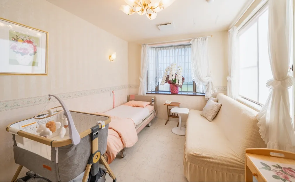 産院の特別室。大きな窓から光が入り、ベッドとソファ、そして赤ちゃん用のベビーベッドが設置されている。通常室よりも広く、快適に過ごせるように配慮された内装。